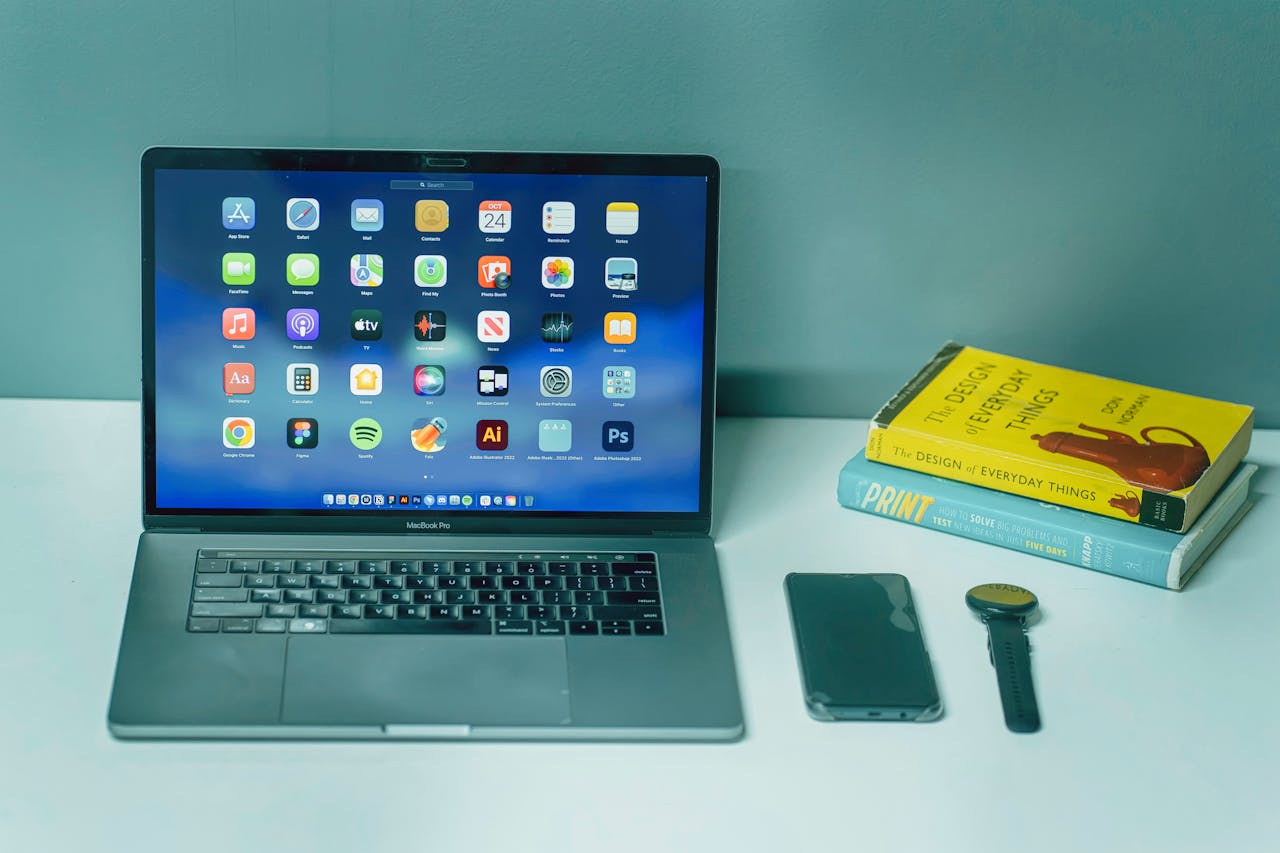 A sleek desk setup featuring a laptop, smartphone, watch, and books for a productive workspace.